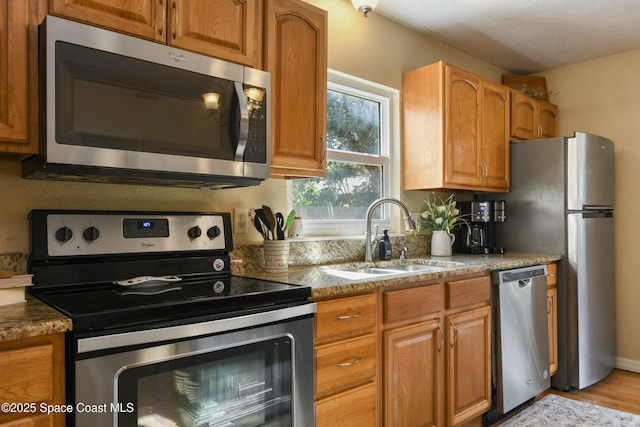 kitchen featuring light stone counters, sink, stainless steel appliances, and light hardwood / wood-style floors