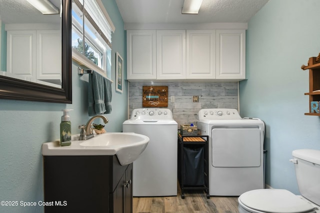 clothes washing area with sink, washer and clothes dryer, light hardwood / wood-style floors, and a textured ceiling