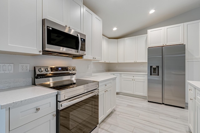 kitchen with white cabinets, light stone countertops, appliances with stainless steel finishes, and lofted ceiling