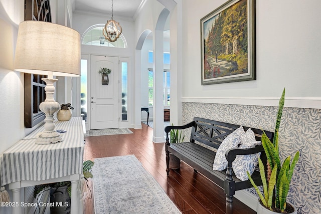 foyer entrance with ornamental molding, dark wood-type flooring, and a chandelier