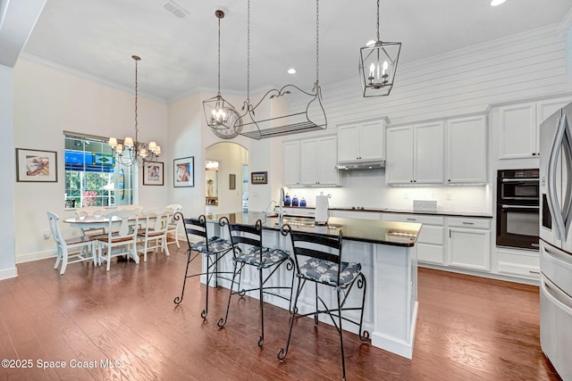 kitchen featuring white cabinetry, decorative light fixtures, and an island with sink