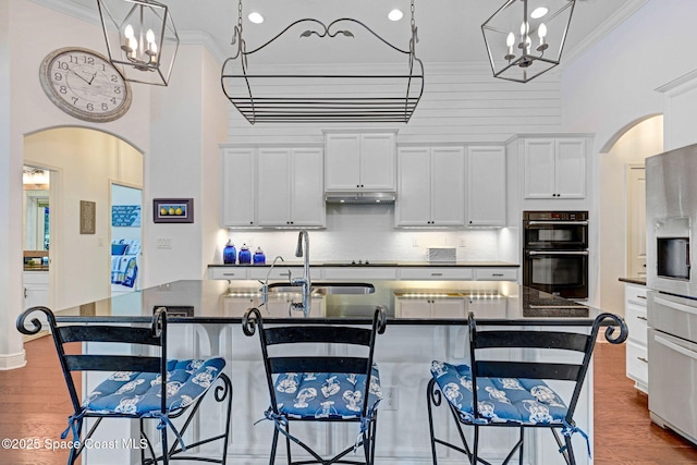 kitchen with sink, crown molding, a kitchen island with sink, white cabinetry, and black double oven