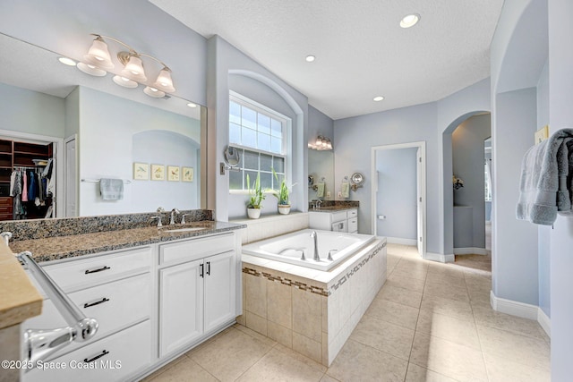 bathroom with tile patterned floors, vanity, a textured ceiling, and tiled tub