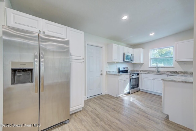 kitchen featuring sink, white cabinetry, light stone counters, stainless steel appliances, and light hardwood / wood-style floors