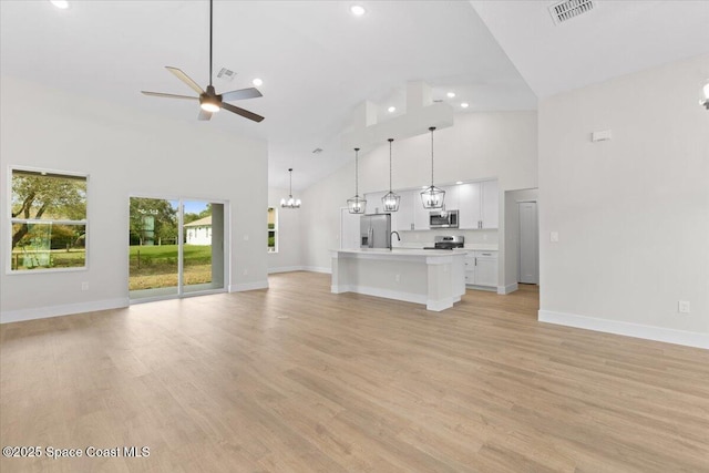 unfurnished living room with high vaulted ceiling, sink, ceiling fan with notable chandelier, and light hardwood / wood-style flooring