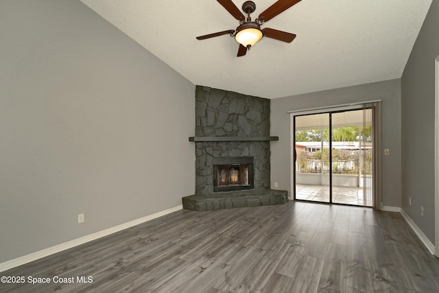 unfurnished living room with ceiling fan, a stone fireplace, dark wood-type flooring, and a textured ceiling