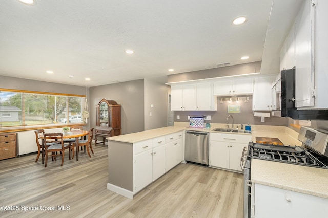 kitchen featuring kitchen peninsula, appliances with stainless steel finishes, sink, white cabinetry, and light hardwood / wood-style floors