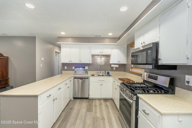 kitchen with white cabinetry, stainless steel appliances, sink, kitchen peninsula, and light wood-type flooring