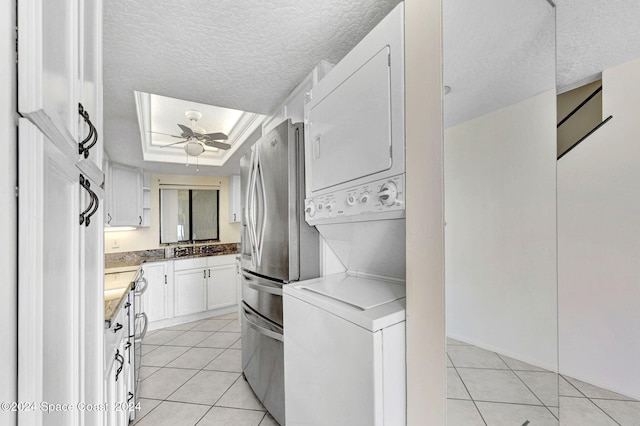 laundry area featuring stacked washing maching and dryer, laundry area, light tile patterned flooring, ceiling fan, and a textured ceiling