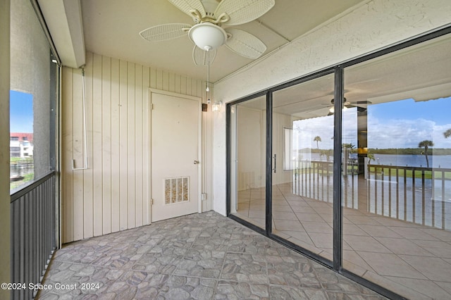 unfurnished sunroom with plenty of natural light, ceiling fan, and a water view