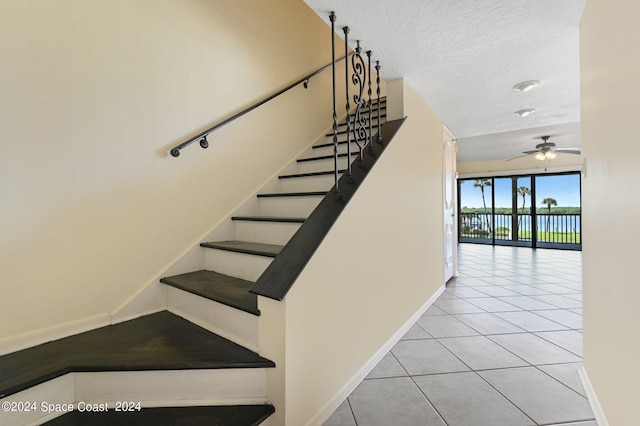 staircase featuring tile patterned floors, baseboards, a textured ceiling, and ceiling fan