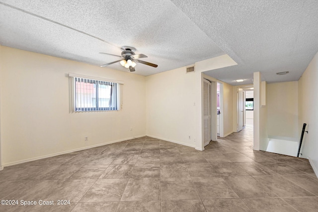 empty room with visible vents, a textured ceiling, baseboards, and a ceiling fan