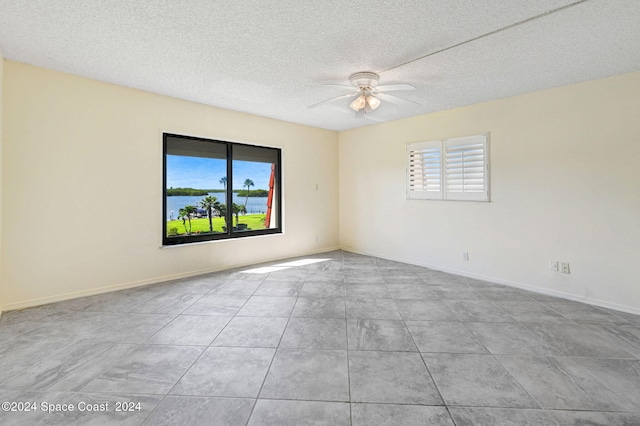 empty room with ceiling fan, light tile patterned floors, and a textured ceiling