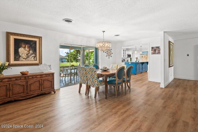 dining area with an inviting chandelier, a textured ceiling, and light wood-type flooring