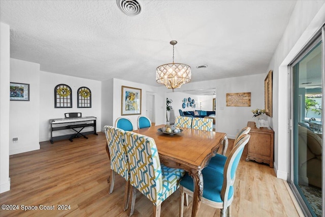 dining space with a textured ceiling, a chandelier, and light hardwood / wood-style flooring