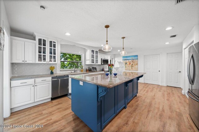 kitchen featuring white cabinetry, hanging light fixtures, a center island, stainless steel appliances, and light stone countertops