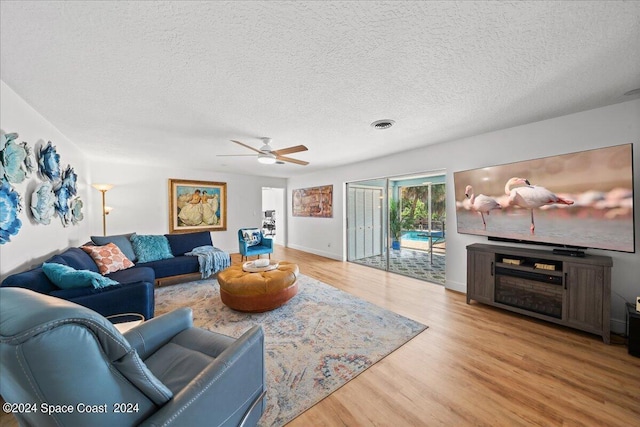 living room with ceiling fan, a textured ceiling, and light wood-type flooring