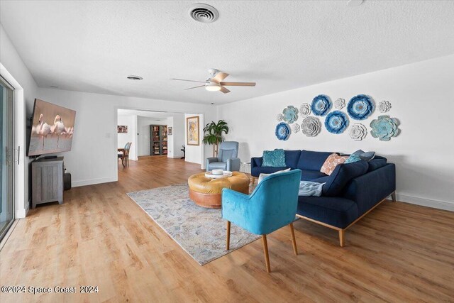 living room with ceiling fan, a textured ceiling, and light wood-type flooring