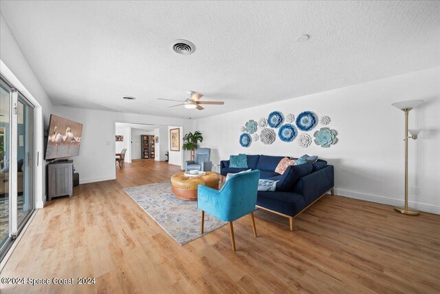 living room with hardwood / wood-style flooring, ceiling fan, and a textured ceiling