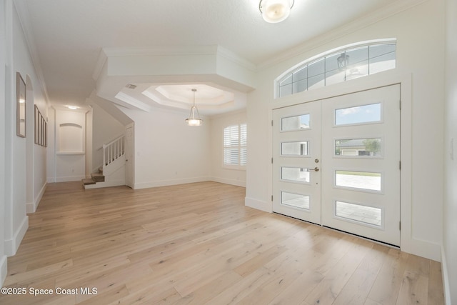 entrance foyer with french doors, ornamental molding, light hardwood / wood-style flooring, and a tray ceiling