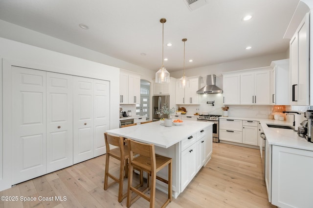 kitchen with wall chimney exhaust hood, a center island, pendant lighting, stainless steel appliances, and white cabinets