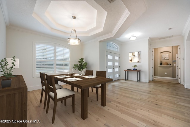 dining area with a raised ceiling, crown molding, light hardwood / wood-style floors, and french doors