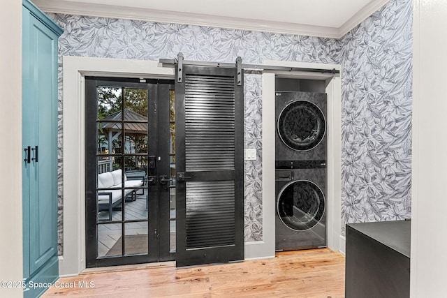 laundry room featuring stacked washer and dryer, crown molding, wood-type flooring, and a barn door