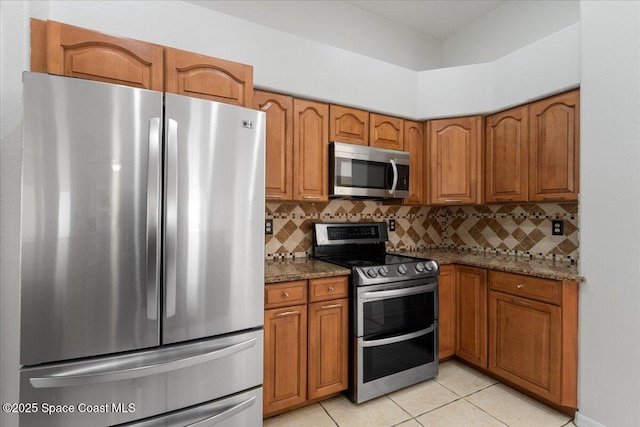 kitchen with light tile patterned floors, decorative backsplash, stainless steel appliances, and dark stone counters