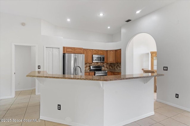 kitchen featuring light tile patterned flooring, appliances with stainless steel finishes, tasteful backsplash, a kitchen breakfast bar, and a center island with sink