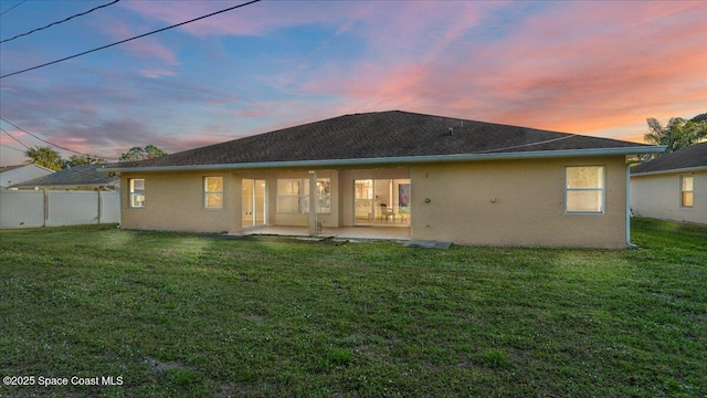 back house at dusk with a yard and a patio