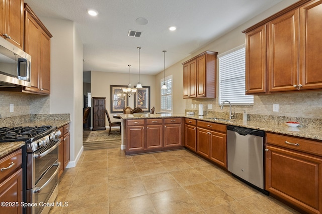 kitchen featuring light stone countertops, sink, decorative light fixtures, kitchen peninsula, and stainless steel appliances