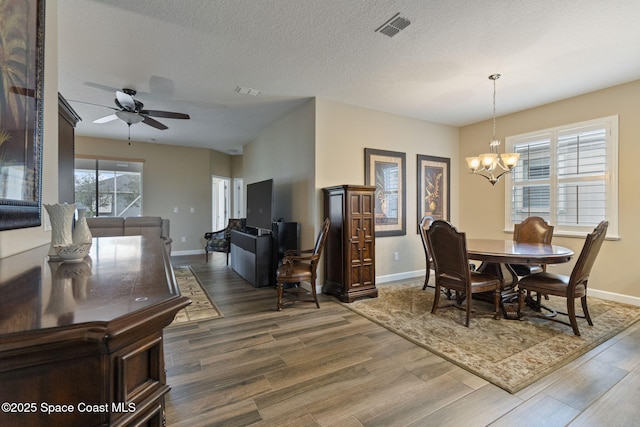 dining room with ceiling fan with notable chandelier, a textured ceiling, and dark hardwood / wood-style flooring