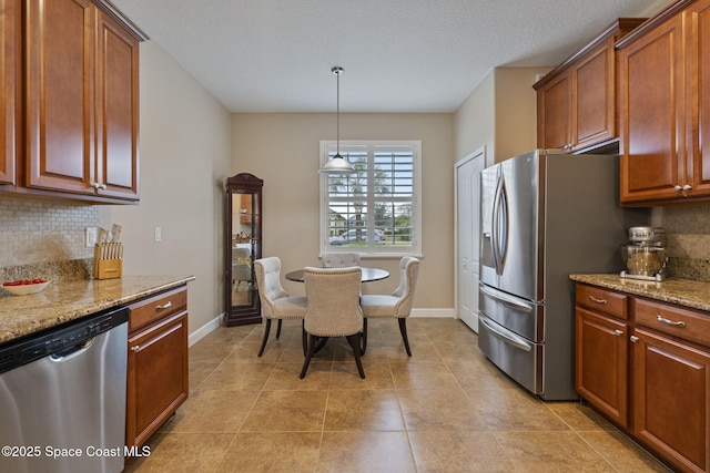 kitchen with appliances with stainless steel finishes, light tile patterned floors, decorative light fixtures, backsplash, and light stone counters