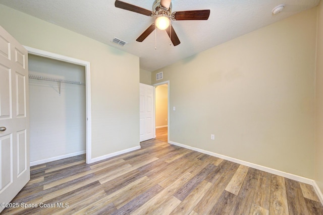 unfurnished bedroom featuring ceiling fan, a textured ceiling, a closet, and light wood-type flooring