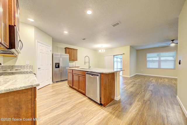 kitchen featuring sink, light wood-type flooring, a textured ceiling, a center island with sink, and stainless steel appliances