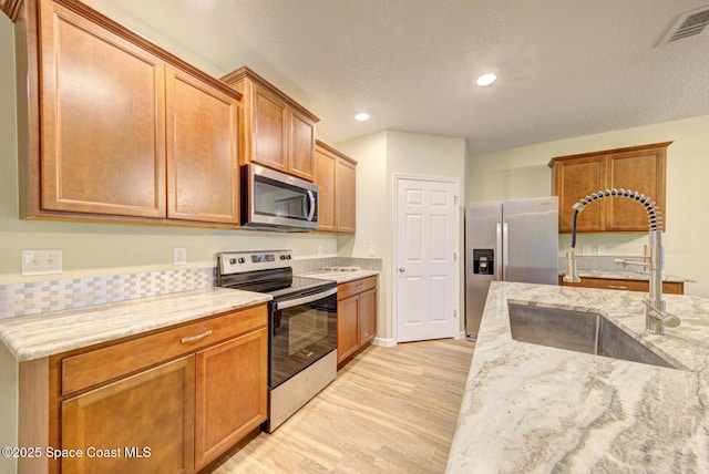 kitchen featuring appliances with stainless steel finishes, sink, light wood-type flooring, light stone countertops, and a textured ceiling