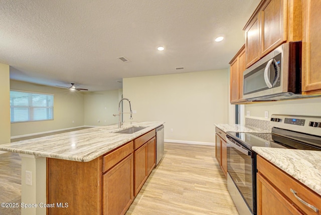 kitchen featuring light hardwood / wood-style flooring, sink, light stone countertops, an island with sink, and stainless steel appliances