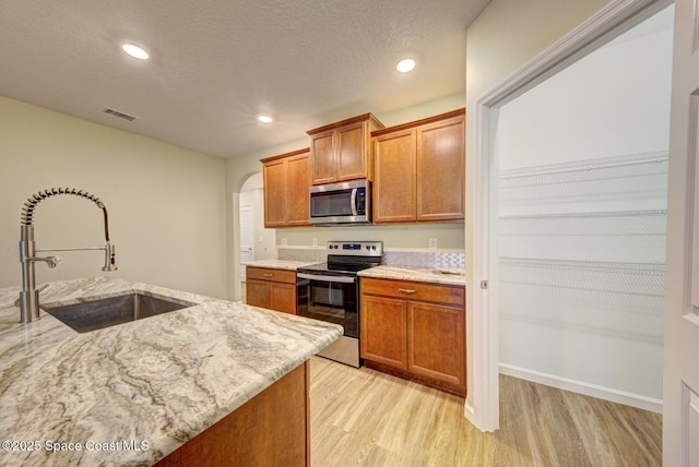 kitchen featuring light hardwood / wood-style flooring, sink, light stone counters, a textured ceiling, and stainless steel appliances