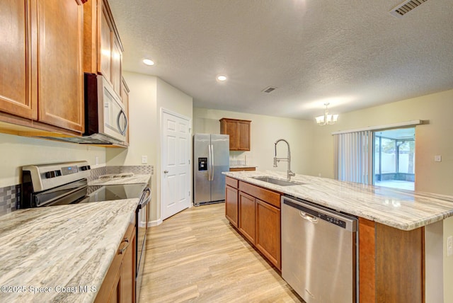 kitchen with sink, a kitchen island with sink, a textured ceiling, and stainless steel appliances