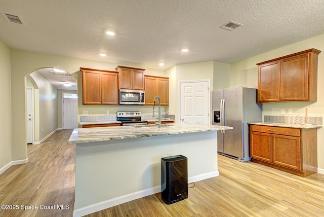 kitchen with sink, light wood-type flooring, stainless steel appliances, and a kitchen island with sink