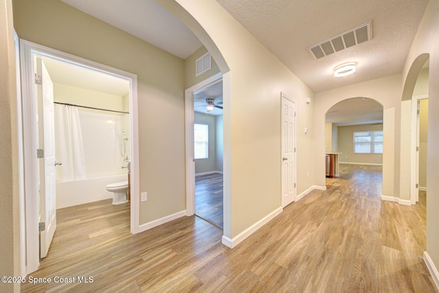 hall with light wood-type flooring and a textured ceiling