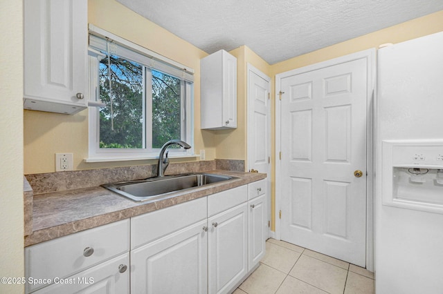 kitchen with white cabinetry, sink, white refrigerator with ice dispenser, light tile patterned floors, and a textured ceiling