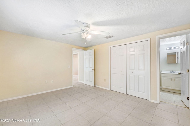 unfurnished bedroom featuring sink, light tile patterned floors, ceiling fan, ensuite bathroom, and a closet