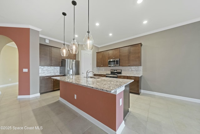 kitchen with light stone counters, hanging light fixtures, light tile patterned floors, appliances with stainless steel finishes, and an island with sink