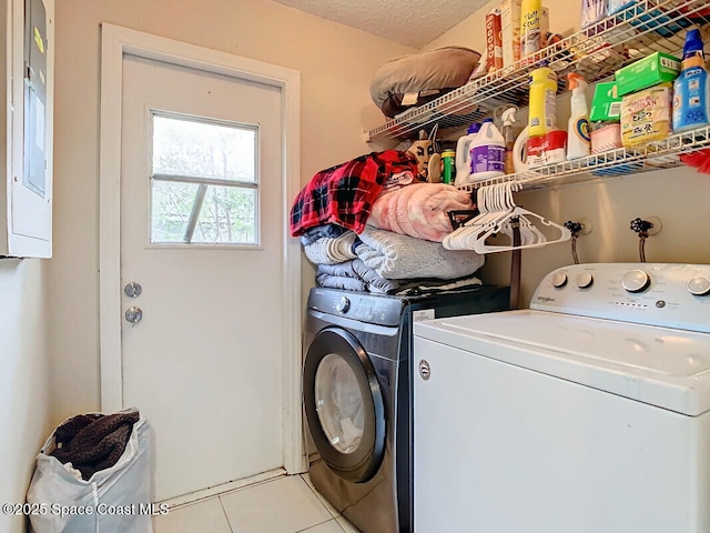 laundry area featuring electric panel, washing machine and dryer, a textured ceiling, and light tile patterned floors