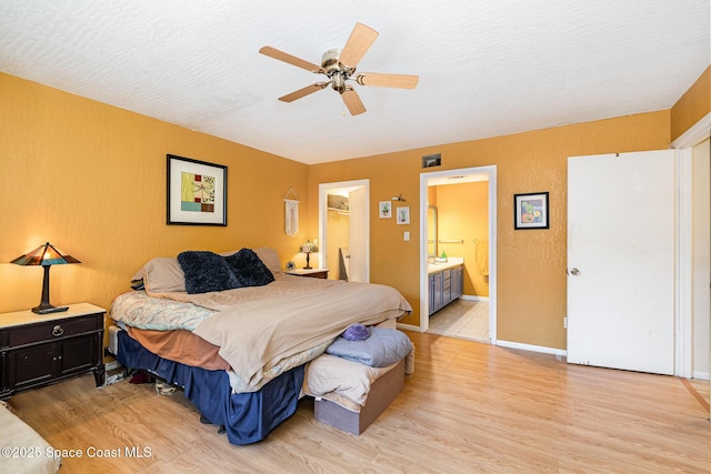 bedroom featuring connected bathroom, a walk in closet, light hardwood / wood-style floors, a textured ceiling, and a closet