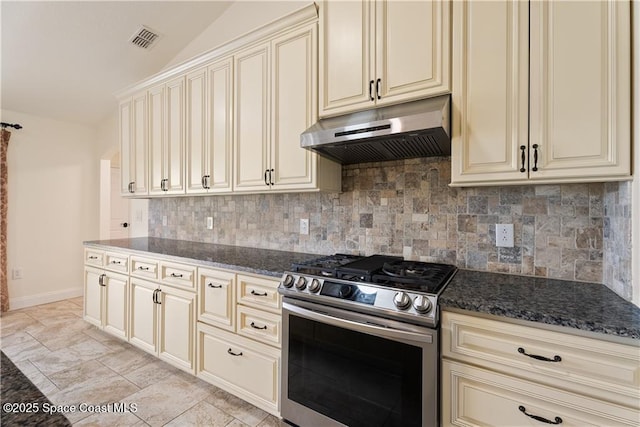 kitchen featuring lofted ceiling, stainless steel gas range, tasteful backsplash, dark stone countertops, and cream cabinetry