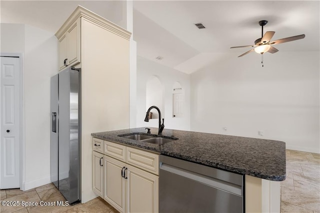 kitchen with lofted ceiling, sink, appliances with stainless steel finishes, dark stone counters, and cream cabinetry