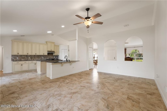 kitchen with lofted ceiling, kitchen peninsula, ceiling fan, cream cabinets, and decorative backsplash