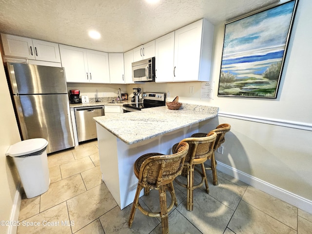 kitchen featuring a breakfast bar, stainless steel appliances, a textured ceiling, white cabinets, and kitchen peninsula